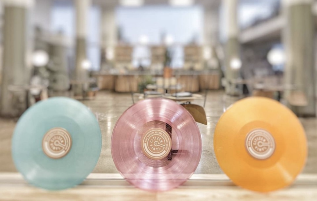 a picture of citizen vinyl and session cafe with an eggshell blue, transparent rose, and light orange vinyl records standing up in the foreground