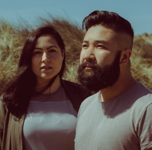 Two people shown from the chest up. Both have dark hair and gray t-shirts.