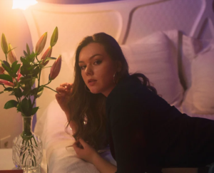 A woman lies on a couch facing a vase of flowers.