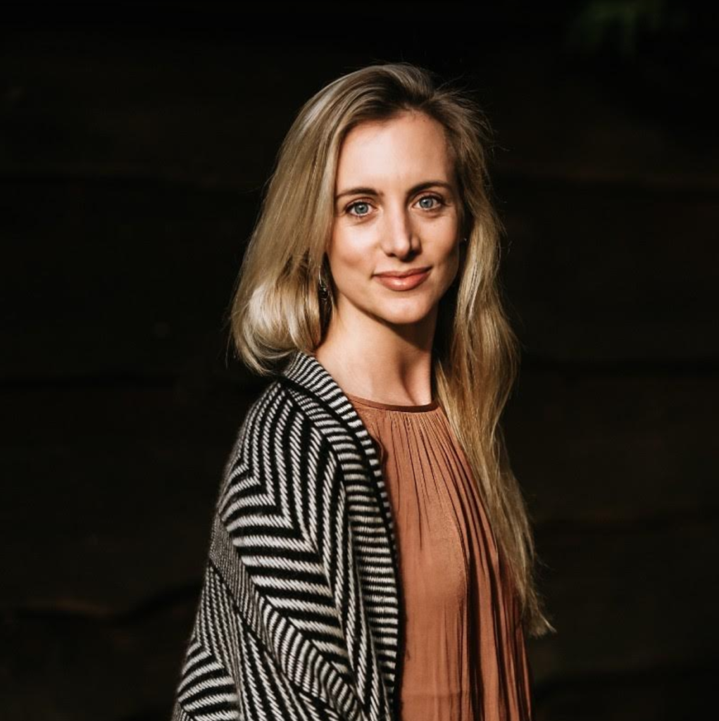 A woman wearing a brown shirt and black and white sweater smiles at the camera.