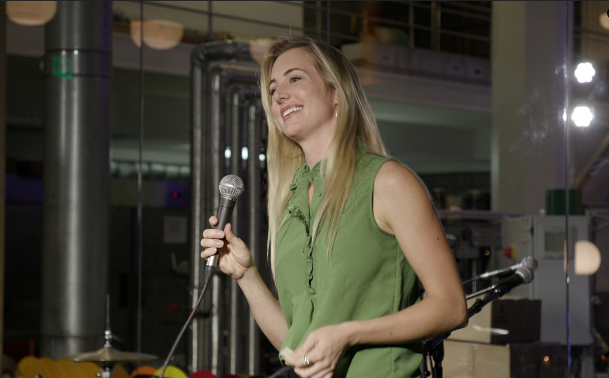 A woman wearing a green shirt speaks into a microphone at an event.
