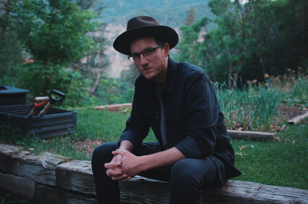 Singer-songwriter Andy Sydow sitting on a stone wall.